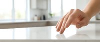 Woman's hand touching clean white kitchen countertop surface, representing hygiene, cleanliness and domestic sanitation for home care and kitchen design projects.