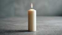 Single white pillar candle burning with bright flame on concrete surface creating peaceful ambiance for meditation, spa treatments, and relaxation rituals.