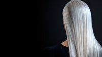 Platinum blonde straight hair on dark background, rear view of woman with silver white long hairstyle showing professional salon coloring result.