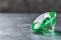 Brilliant emerald green crystal gemstone on gray concrete background with soft reflection and dramatic lighting for luxury jewelry design concepts.