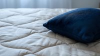 Dark blue cushion resting on quilted white bedding, showcasing comfortable bedroom decor and textile design for home furnishing and interior styling projects.