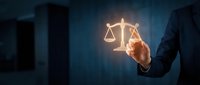 Businessman in dark suit touching glowing scales of justice symbol against blurred cityscape background, representing legal services, law firm, compliance, and corporate governance concepts.