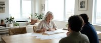 Senior Caucasian businesswoman leading meeting with diverse team in bright modern office discussing documents and strategy planning session.
