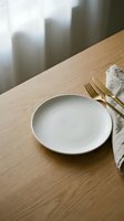 Empty white plate with gold cutlery and linen napkin on wooden table with city skyline view, suitable for restaurant, dining, and hospitality design projects.