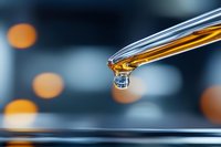 Glass pipette dropping golden liquid sample in laboratory setting with blurred bokeh lights background for scientific research and analysis applications.
