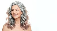 Mature woman with long wavy silver and rose-toned hair, fair complexion, smiling against white background. Suitable for beauty, haircare, aging gracefully, and wellness campaigns.