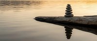 Zen stone stack balanced on driftwood log over calm water at golden sunset creating peaceful reflection for meditation and mindfulness concepts.