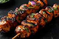 Grilled chicken tikka kebabs with charred edges and fresh herbs on wooden skewers, close up view against dark background. Traditional Indian cuisine.
