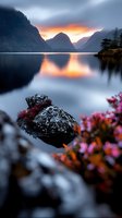 Serene alpine lake at sunrise with snow-covered rocks, vibrant wildflowers, and misty mountain peaks reflected in calm waters. Perfect for nature and travel backgrounds.