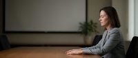 Professional businesswoman in gray suit sitting at conference table in modern office boardroom for corporate meetings and presentations.