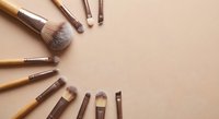 Professional makeup brushes with wooden handles arranged on neutral beige background with copy space for beauty and cosmetics applications.