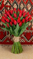 Fresh red tulip bouquet tied with twine against ethnic patterned carpet background, combining natural floral beauty with traditional textile design elements.