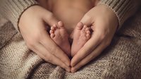 Adult hands forming heart shape around newborn baby feet, maternity and family bonding concept.