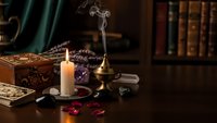 Mystical fortune telling setup with burning candle, tarot cards, crystal ball and vintage books creating atmospheric divination scene for spiritual practices.