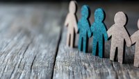 Paper cutout figures in white and blue tones standing together on rustic wooden surface, representing community, diversity, and social connection in minimalist style.