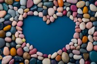 Colorful smooth pebbles and stones arranged in heart shape on blue background, creating romantic natural composition for wellness, spa and meditation concepts.