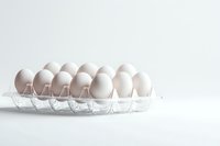 Fresh white eggs arranged in clear plastic container on bright background, minimalist food photography composition with copy space for healthy eating concept.