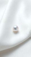 Single lustrous pearl resting on soft white fabric with gentle folds, showcasing luxury jewelry and elegant design elements for premium branding.