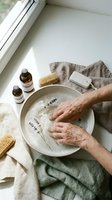 Senior woman hands soaking in lavender milk bath bowl with natural spa accessories and essential oils for relaxation and skincare routine.