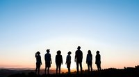 Silhouettes of diverse group of people standing together on hilltop at sunset, representing unity, teamwork, and community connection for business and social concepts.