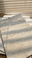 Natural handmade paper sheets with organic texture and fibers scattered on wooden surface near window with warm sunlight and venetian blind shadows.
