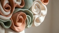 Elegant handmade paper roses in soft pastel colors including sage green, peach and cream tones arranged in artistic bouquet for wedding decor and crafting.