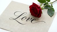 Red rose resting on a linen card with elegant calligraphy word Love, romantic symbol for Valentine's Day, wedding, and anniversary designs.