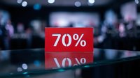 Red sale sign displaying 70% discount on glass counter in blurred retail store, reflecting on surface for shopping promotion concept.