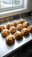 Freshly baked round artisan bread rolls with golden-brown crusts arranged on parchment paper on a kitchen windowsill, ideal for bakery, food, and culinary content.