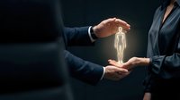 Professional businessman in dark suit protecting glowing human figure with cupped hands representing healthcare insurance coverage and employee protection.