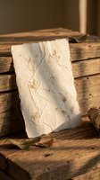 Handmade paper sheet with pressed botanical elements on rustic wooden planks in warm natural lighting for craft and stationery projects.