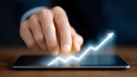 Glowing upward arrow chart emerging from digital tablet screen with hand pointing, representing business growth and financial success in modern technology.