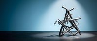 Tangled mass of metal crutches and walking aids creating abstract sculpture against dramatic blue gradient background with spotlight illumination.