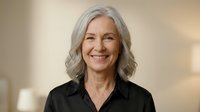 Confident mature Caucasian businesswoman with gray hair smiling warmly in professional black attire against soft blurred office background for corporate use.