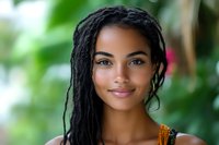 Young African American woman with dreadlocks smiling outdoors in natural green environment, portrait of confident female with braided hairstyle and warm expression.