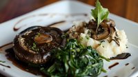Grilled portobello mushroom with mashed potatoes, sauteed spinach and balsamic reduction on white plate, garnished with fresh herbs and sauce drizzle.