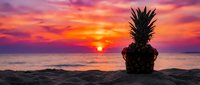 Pineapple wearing sunglasses on sandy beach at vibrant tropical sunset, ocean horizon glowing red and orange, fun summer vacation concept.