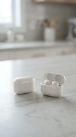 White wireless earbuds in charging case on marble kitchen counter with blurred modern interior background for technology and lifestyle concepts.