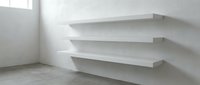 Modern white floating shelves mounted on wall in minimalist interior room with concrete floor and natural light from window.