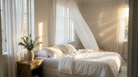 Cozy bedroom interior with white bedding, flowing curtains and warm natural light creating peaceful morning atmosphere for home decor and lifestyle.