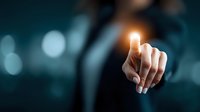 Business person pointing finger with glowing light effect against dark background, symbolizing innovation, choice, or digital transformation in corporate environment.
