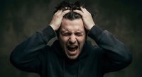 Stressed middle-aged Caucasian man screaming with hands on head expressing frustration, mental breakdown, anxiety and overwhelming emotions against dark background.