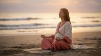 Young woman meditating in lotus pose on beach at sunset, practicing mindfulness and yoga by ocean waves. Peaceful wellness lifestyle and spiritual relaxation.