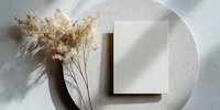 Minimalist blank card mockup with dried pampas grass on textured round plate, neutral beige tones for elegant stationery presentation.