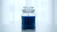 Blue scented candle in glass jar with cotton wick on white background for home decor and aromatherapy relaxation.