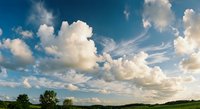 Dramatic cloudy sky with puffy white clouds over green countryside landscape. Natural outdoor scenery for environmental and weather concepts.