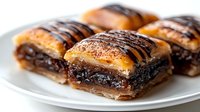 Flaky pastry squares filled with rich chocolate and nuts, drizzled with dark chocolate glaze on white plate for bakery menu and dessert photography.