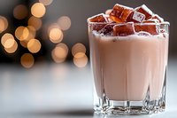 Creamy chocolate cocktail with ice cubes in glass against blurred warm bokeh lights, perfect for beverage and bar design projects.