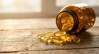 Amber glass bottle with yellow omega-3 fish oil capsules spilling onto wooden surface in bright natural light for health and wellness supplement concepts.