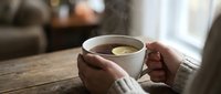 Person holding warm tea cup with lemon slice on wooden table in cozy home interior, relaxation and comfort beverage concept for lifestyle and wellness design.